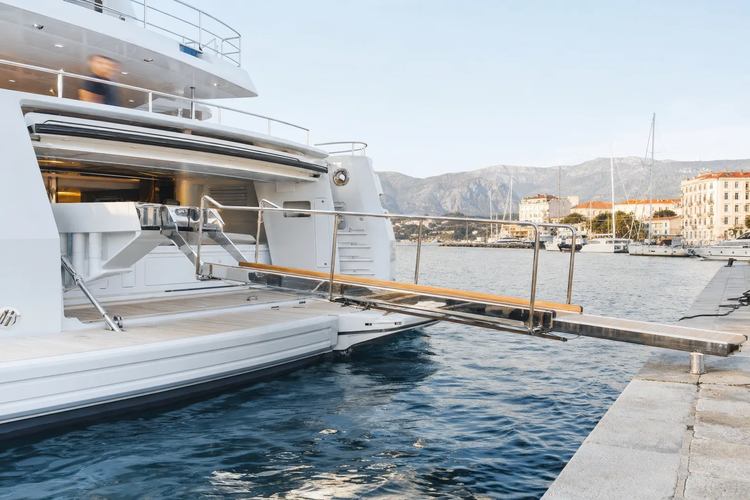 A polished stainless telescopic passerelle extended from the stern of a large yacht to a stone quay